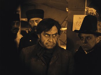 Movie still from “The Cabinet of Dr. Caligari” (1920), directed by Robert Wiene – A group of men standing next to each other in a dark room; Medium shot, Over the shoulder angle