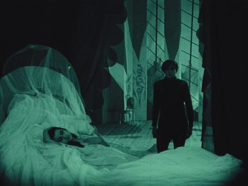 Movie still from “The Cabinet of Dr. Caligari” (1920), directed by Robert Wiene – A woman standing next to a bed in a dark room; Wide shot, High angle