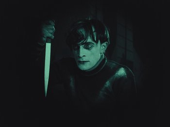Movie still from “The Cabinet of Dr. Caligari” (1920), directed by Robert Wiene – A man holding a knife in a dark room; Medium shot, High angle