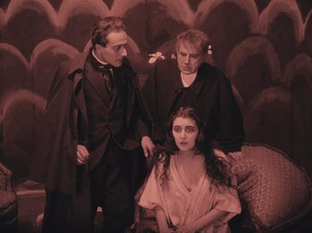 Movie still from “The Cabinet of Dr. Caligari” (1920), directed by Robert Wiene – A man and two women are sitting on a couch; Medium shot, High angle