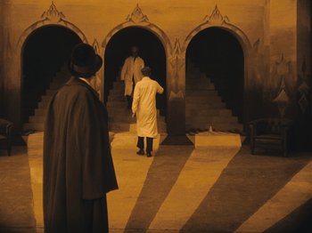 Movie still from “The Cabinet of Dr. Caligari” (1920), directed by Robert Wiene – Two men in white coats are standing in front of stairs; Wide shot, High angle