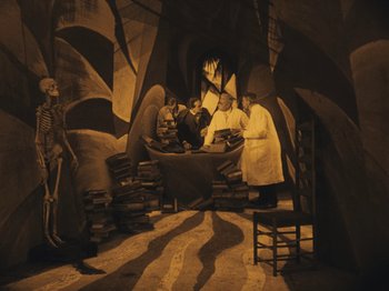 Movie still from “The Cabinet of Dr. Caligari” (1920), directed by Robert Wiene – A group of people standing around a table; Wide shot, High angle