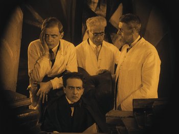 Movie still from “The Cabinet of Dr. Caligari” (1920), directed by Robert Wiene – A group of men standing next to each other in a room; Medium shot, Low angle