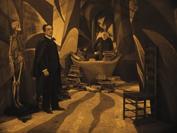Movie still from “The Cabinet of Dr. Caligari” (1920), directed by Robert Wiene – Two men standing next to each other in a room; Wide shot, High angle