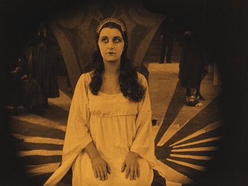 Movie still from “The Cabinet of Dr. Caligari” (1920), directed by Robert Wiene – A woman in a white dress sitting on a chair; Medium shot, High angle