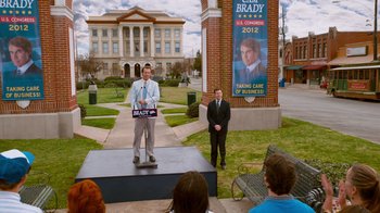 Movie still from “The Campaign” (2012), directed by Jay Roach – Two men standing on a stage in front of a building; Extreme Wide shot, High angle