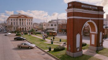 Movie still from “The Campaign” (2012), directed by Jay Roach – People are walking on the grass near a tall brick tower; Extreme Wide shot, High angle
