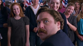 Movie still from “The Campaign” (2012), directed by Jay Roach – A group of people standing in front of an american flag; Close Up shot, Over the shoulder angle