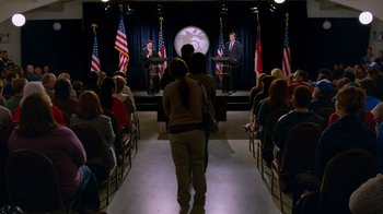 Movie still from “The Campaign” (2012), directed by Jay Roach – A couple of people standing in front of a podium; Wide shot, High angle