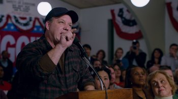 Movie still from “The Campaign” (2012), directed by Jay Roach – A man is speaking at a podium in front of a crowd of onlookers; Medium shot, Over the shoulder angle