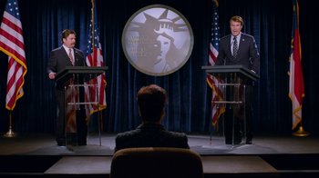 Movie still from “The Campaign” (2012), directed by Jay Roach – Two men are sitting in front of a microphone; Wide shot, High angle