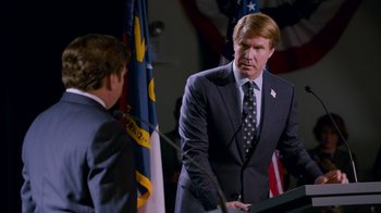 Movie still from “The Campaign” (2012), directed by Jay Roach – A man in a suit and tie standing in front of a podium; Medium shot, Over the shoulder angle