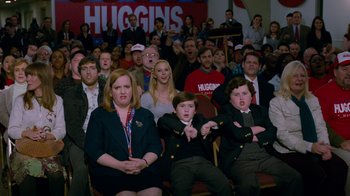 Movie still from “The Campaign” (2012), directed by Jay Roach – A group of people sitting in front of a crowd; Medium shot, Over the shoulder angle