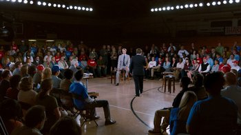 Movie still from “The Campaign” (2012), directed by Jay Roach – A man in a suit and tie standing in front of an audience; Wide shot, High angle