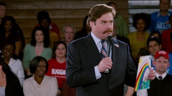 Movie still from “The Campaign” (2012), directed by Jay Roach – A man in a suit and tie holding a microphone; Medium shot, High angle