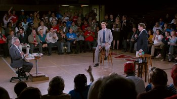 Movie still from “The Campaign” (2012), directed by Jay Roach – A man sitting on top of a chair in front of a crowd; Wide shot, High angle