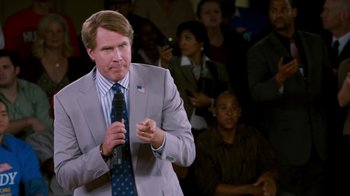 Movie still from “The Campaign” (2012), directed by Jay Roach – A man in a gray suit is holding a microphone; Medium shot, High angle