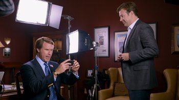 Movie still from “The Campaign” (2012), directed by Jay Roach – A man in a suit and tie taking a picture of another man in a suit and tie; Medium shot, Over the shoulder angle