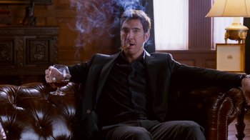 Movie still from “The Campaign” (2012), directed by Jay Roach – A man sitting on a couch smoking a cigarette; Medium shot, Low angle
