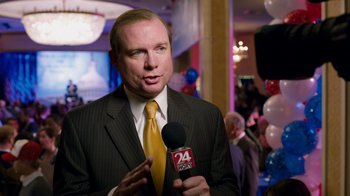 Movie still from “The Campaign” (2012), directed by Jay Roach – A man wearing a suit and tie holding a microphone; Close Up shot, Over the shoulder angle