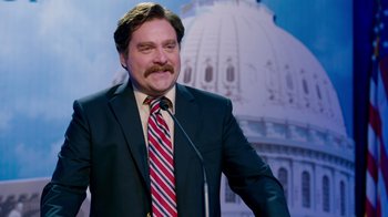 Movie still from “The Campaign” (2012), directed by Jay Roach – A man in a suit and tie standing in front of a microphone; Medium shot, Low angle