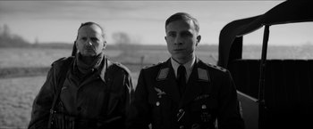 Movie still from “The Captain” (2017), directed by Robert Schwentke – A man in a military uniform standing next to another man; Medium shot, Over the shoulder angle