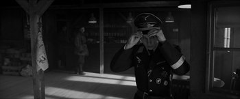 Movie still from “The Captain” (2017), directed by Robert Schwentke – A man in a military uniform adjusts his hat; Medium shot, Over the shoulder angle