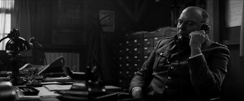 Movie still from “The Captain” (2017), directed by Robert Schwentke – A man sitting at a table in a room; Medium shot, Low angle