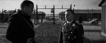Movie still from “The Captain” (2017), directed by Robert Schwentke – Two men in military uniforms standing next to each other in front of barbed wire fence; Medium shot, Over the shoulder angle