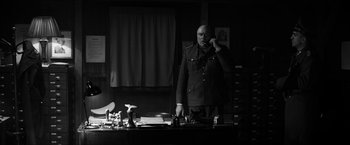 Movie still from “The Captain” (2017), directed by Robert Schwentke – A man standing in front of a desk talking on a phone; Medium shot, Low angle