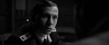 Movie still from “The Captain” (2017), directed by Robert Schwentke – A man in a suit and tie looking at the camera; Close Up shot, Over the shoulder angle