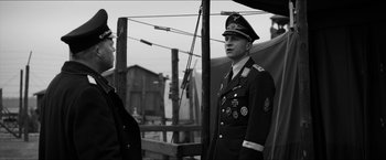 Movie still from “The Captain” (2017), directed by Robert Schwentke – A man in a military uniform standing next to another man; Medium shot, Over the shoulder angle