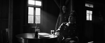 Movie still from “The Captain” (2017), directed by Robert Schwentke – A man sitting at a table in front of a glass of alcohol; Medium shot, Over the shoulder angle