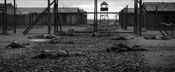 Movie still from “The Captain” (2017), directed by Robert Schwentke – A black and white photo of a group of people laying on the ground in front of barbed wire; Extreme Wide shot, High angle
