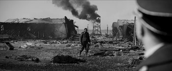 Movie still from “The Captain” (2017), directed by Robert Schwentke – A man standing in the middle of an area with smoke billowing out of the chimney; Wide shot, Low angle
