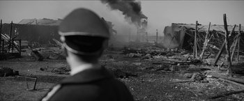 Movie still from “The Captain” (2017), directed by Robert Schwentke – A man standing in front of an industrial area with smoke billowing out of it; Extreme Wide shot, High angle