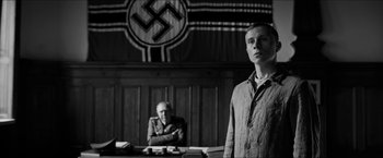 Movie still from “The Captain” (2017), directed by Robert Schwentke – A man standing in front of another man sitting in front of a desk; Medium shot, Low angle