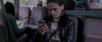 Movie still from “Personal Shopper” (2016), directed by Olivier Assayas – A woman is looking at her cell phone while sitting on a bus; Medium shot, Over the shoulder angle