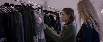 Movie still from “Personal Shopper” (2016), directed by Olivier Assayas – A woman looking at clothes hanging on a rack; Medium shot, Over the shoulder angle