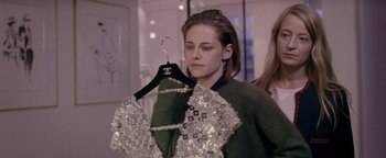 Movie still from “Personal Shopper” (2016), directed by Olivier Assayas – A woman holding onto a dress on top of a hanger; Medium shot, Over the shoulder angle