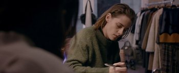 Movie still from “Personal Shopper” (2016), directed by Olivier Assayas – A woman sitting at a table looking at her cell phone; Medium shot, Over the shoulder angle