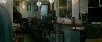 Movie still from “Personal Shopper” (2016), directed by Olivier Assayas – A woman sitting at a bar with her head on a bar stool; Wide shot, High angle