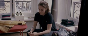Movie still from “Personal Shopper” (2016), directed by Olivier Assayas – A woman sitting on the ground looking at her cell phone; Medium shot, Over the shoulder angle