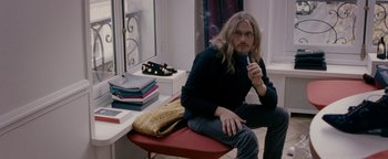 Movie still from “Personal Shopper” (2016), directed by Olivier Assayas – A man sitting on top of a chair holding a cigarette; Medium shot, Over the shoulder angle