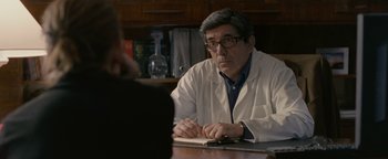 Movie still from “Personal Shopper” (2016), directed by Olivier Assayas – A man in a lab coat sitting at a table; Medium shot, Over the shoulder angle