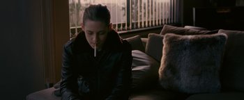 Movie still from “Personal Shopper” (2016), directed by Olivier Assayas – A woman sitting on a couch with a cigarette in her mouth; Medium shot, Over the shoulder angle