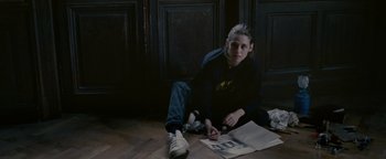 Movie still from “Personal Shopper” (2016), directed by Olivier Assayas – A person sitting on the floor with a pen and a newspaper; Medium shot, High angle