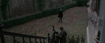 Movie still from “Personal Shopper” (2016), directed by Olivier Assayas – Two people are walking in a park near a railing; Wide shot, High angle