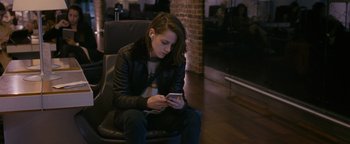 Movie still from “Personal Shopper” (2016), directed by Olivier Assayas – A woman sitting in a chair looking at her cell phone; Medium shot, High angle