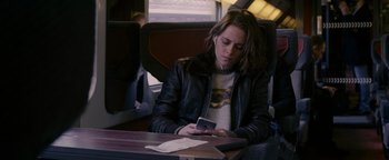 Movie still from “Personal Shopper” (2016), directed by Olivier Assayas – A woman sitting on a train looking at her cell phone; Medium shot, Over the shoulder angle